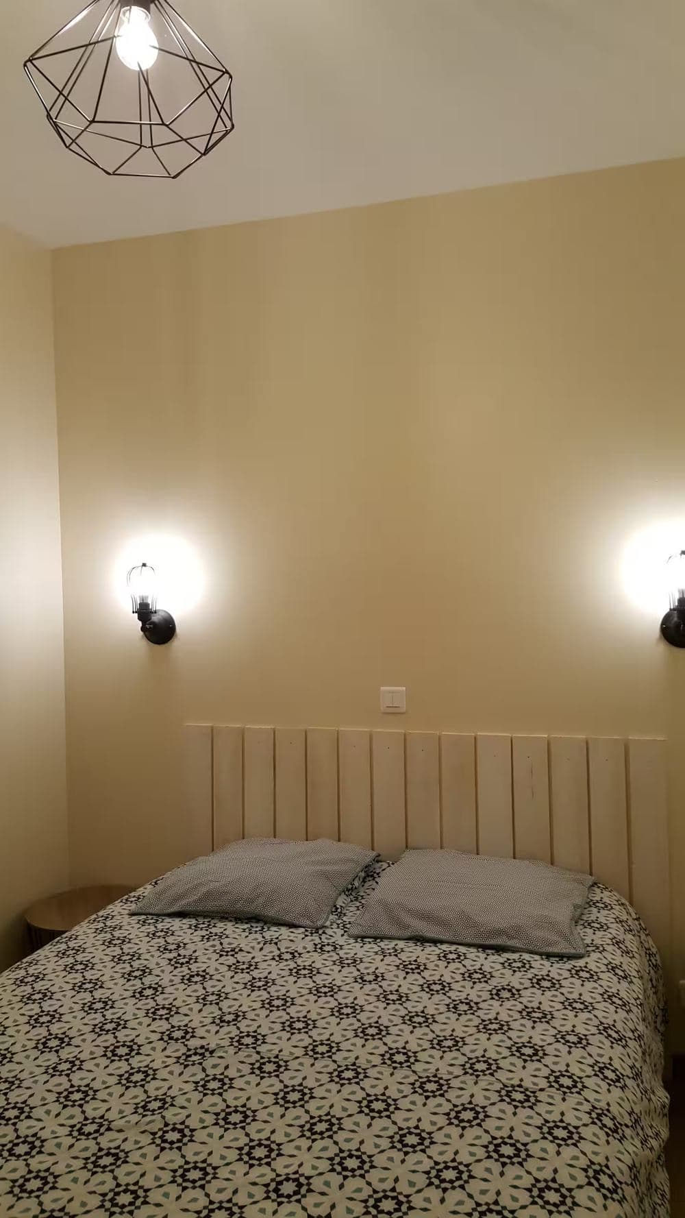 Chambre du gîte, tête de lit en bois clair et appliques murales de part et d'autre du lit double