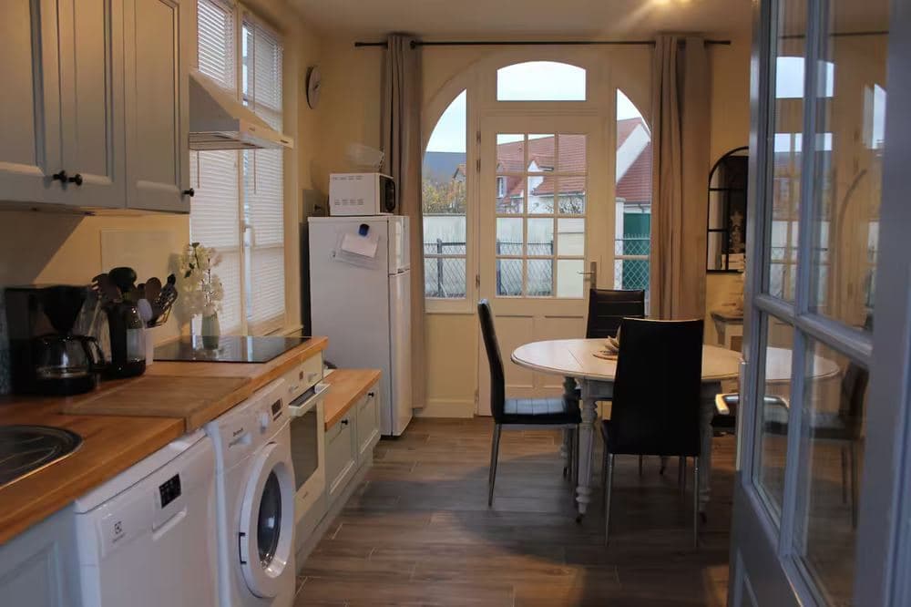 Cuisine équipée du gîte : réfrigérateur, micro-ondes, lave-linge et table de repas devant la porte-fenêtre