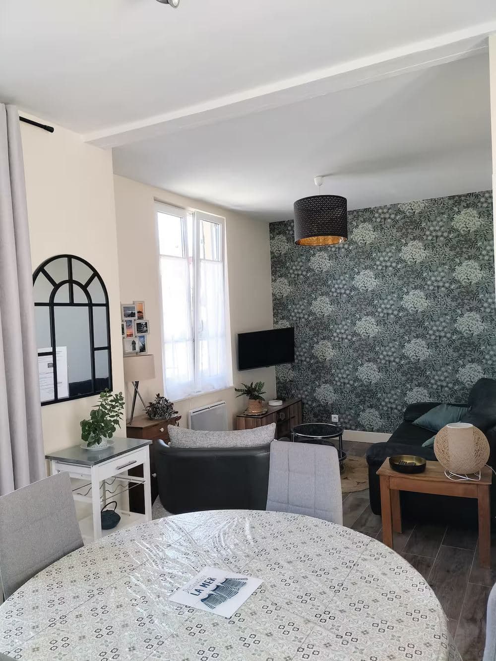 Pièce de vie ouverte sur la salle à manger, avec canapé, télévision et papier peint fleuri